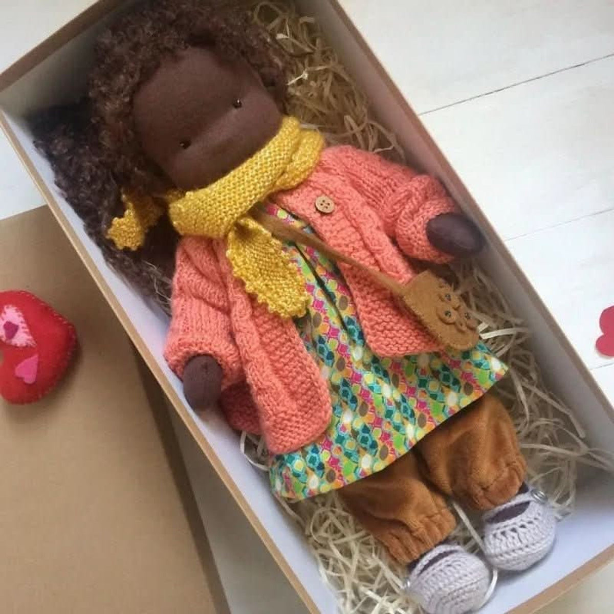 Brown-skinned cloth doll in coral cardigan and yellow scarf
