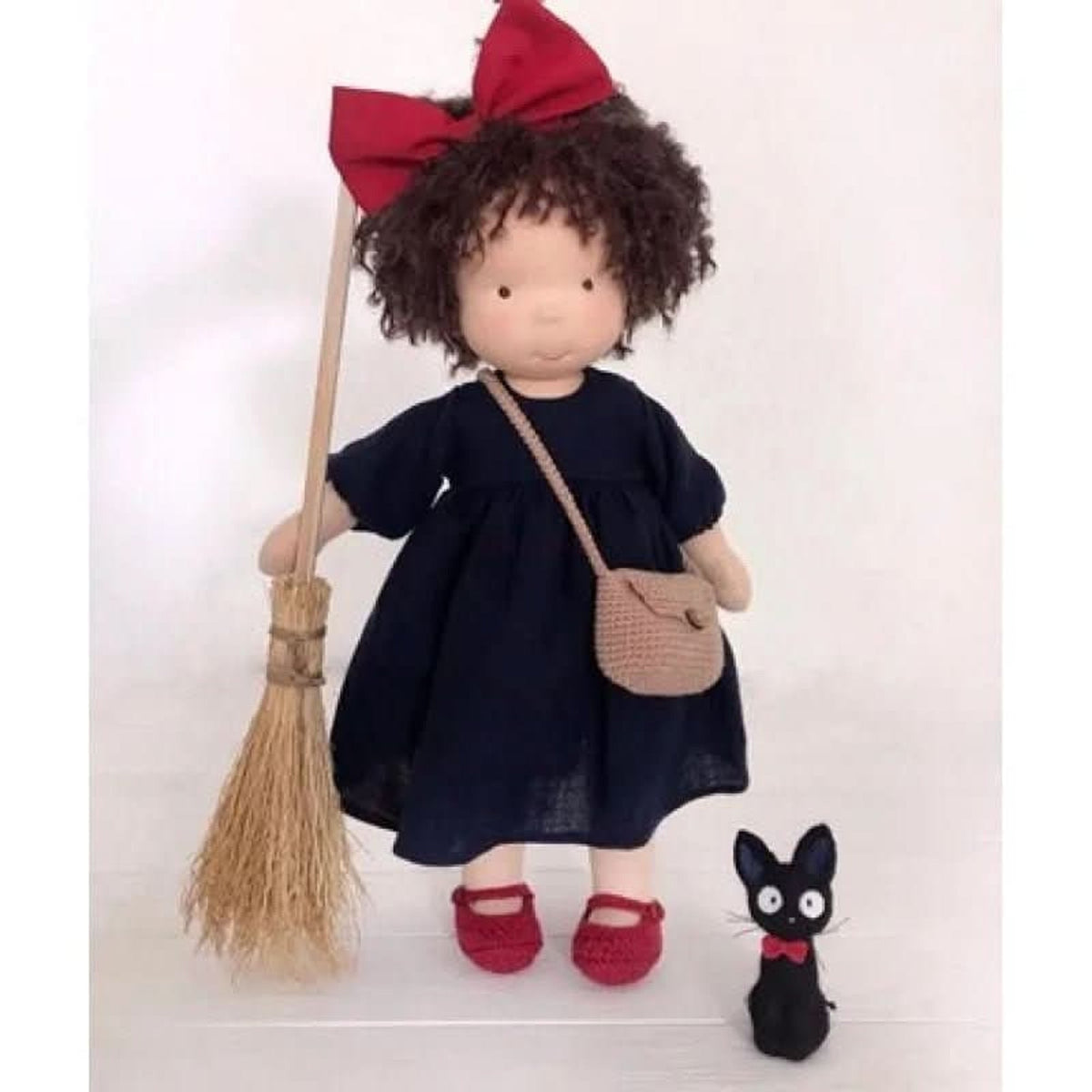 Black-haired cloth doll in navy dress with red hair bow