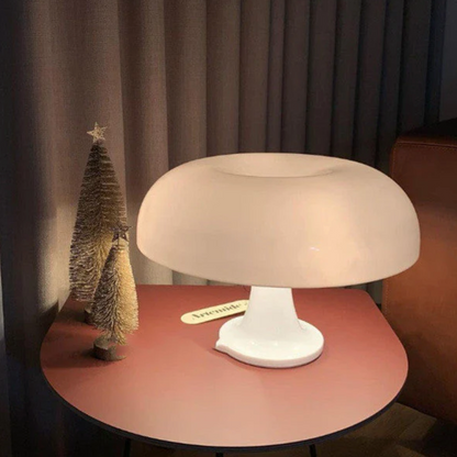 Beige table lamp on a round wooden table with a small decorative tree in the background.