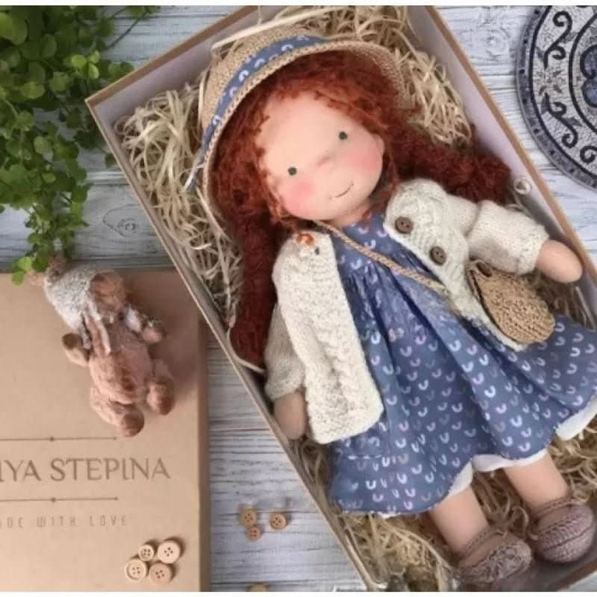 Red-haired cloth doll in blue patterned dress and straw hat