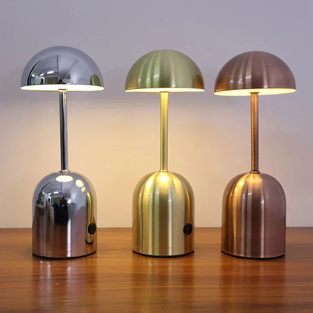 Three metallic table lamps in silver, gold, and bronze on a wooden surface.